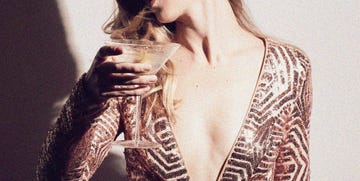 a woman in a gold sequin dress holding a cocktail with her face obscured