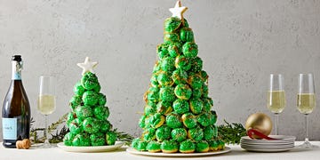 croquembouche in the shape of a christmas tree with green icing and white sprinkles with a sugar cookie star on top