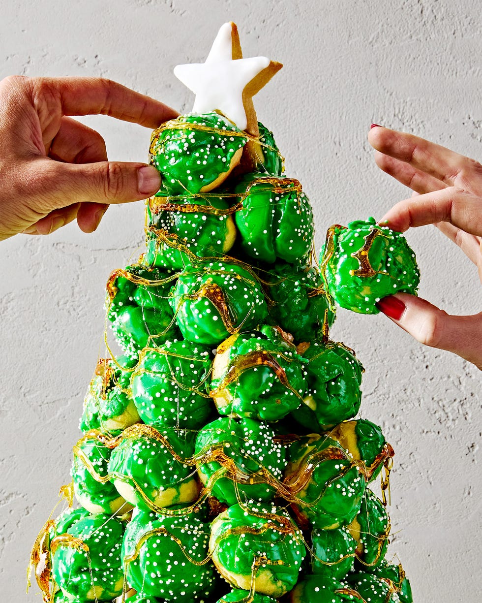 croquembouche in the shape of a christmas tree with green icing and white sprinkles with a sugar cookie star on top