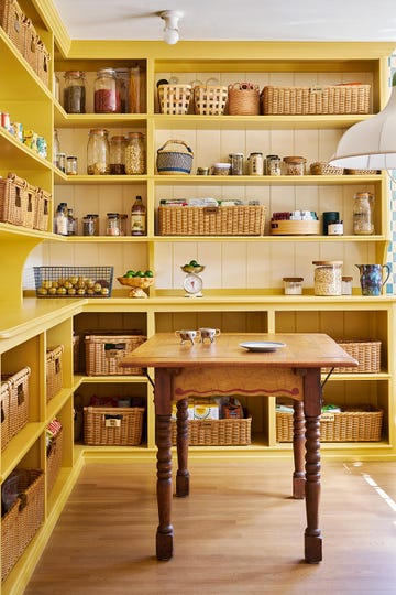 yellow kitchen pantry with large wooden dining table and shelves stocked with baskets and food