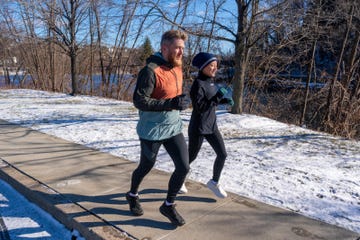 two individuals jogging on a snowy path next to a river