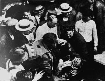 inventor garrett morgan helping responders lift the body of a tunnel disaster victim while wearing his safety hood device on his back