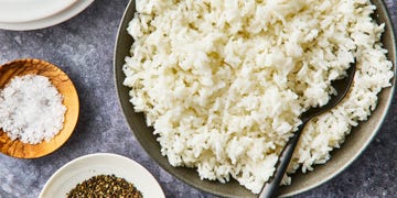 a bowl of white rice with bowls of salt and pepper on the side