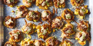 french onion smashed potatoes topped with caramelized onions, gruyere, and thyme on a baking sheet