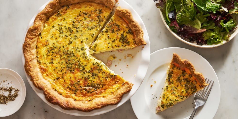 ham and cheese quiche with a slice on a plate beside it and a salad bowl nearby