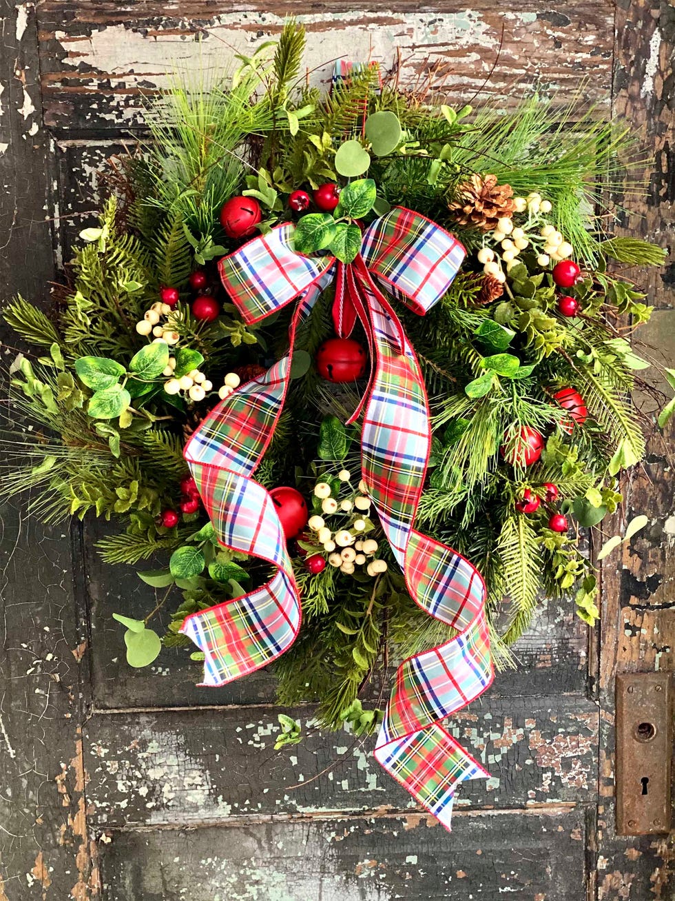 a greenery wreath with red  and white berries plus a large tartan bow