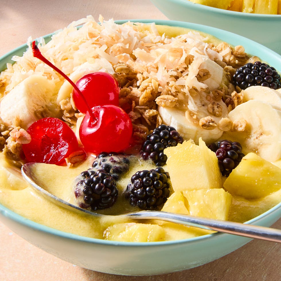 pineapple dole whip smoothie bowl in a blue bowl topped with pineapple, banana, blackberries, cherries, and toasted coconut flakes