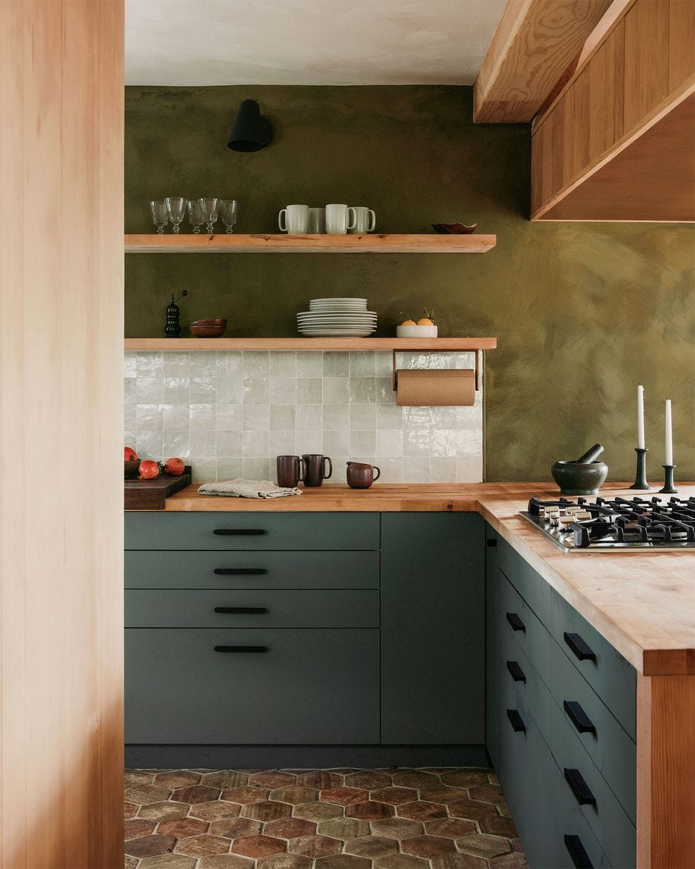 a kitchen with a stove  tiled backsplash in a white color  dark green cabinetry  and a lighter green wall coloring