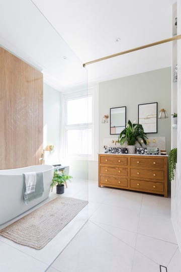 large wooden vanity unit, square terrazzo countertop basins, peace lily, black framed mirrors, white bathtub, fern, bath mat and fluted wooden wall panel