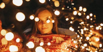 beautiful young woman decorating christmas tree and playing with christmas lights at home