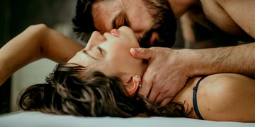 side view photo of a beautiful couple in bed, being gentle and sensual handsome guy with a beard on top of the beautiful brunette is kissing her neck while her eyes are closed making love concept