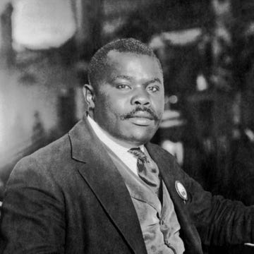 marcus garvey stares at the camera while seated, he wears a suit jacket, vest, collared shirt and tie