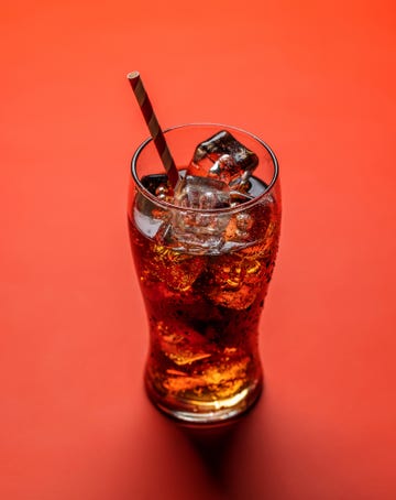 refreshing glass of cola with ice over red background