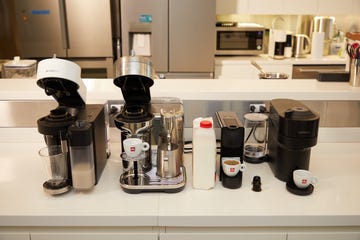 four nespresso machines on a counter with a milk jug, cups of espresso and capsules