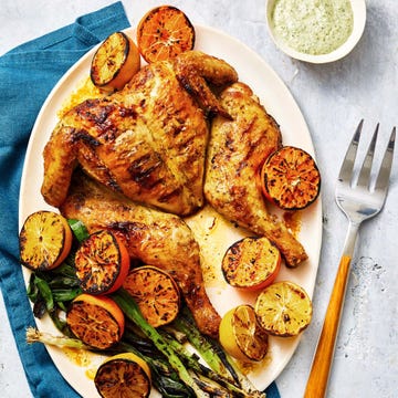 grilled spatchcock chicken with lemons and green scallions served on a white plate