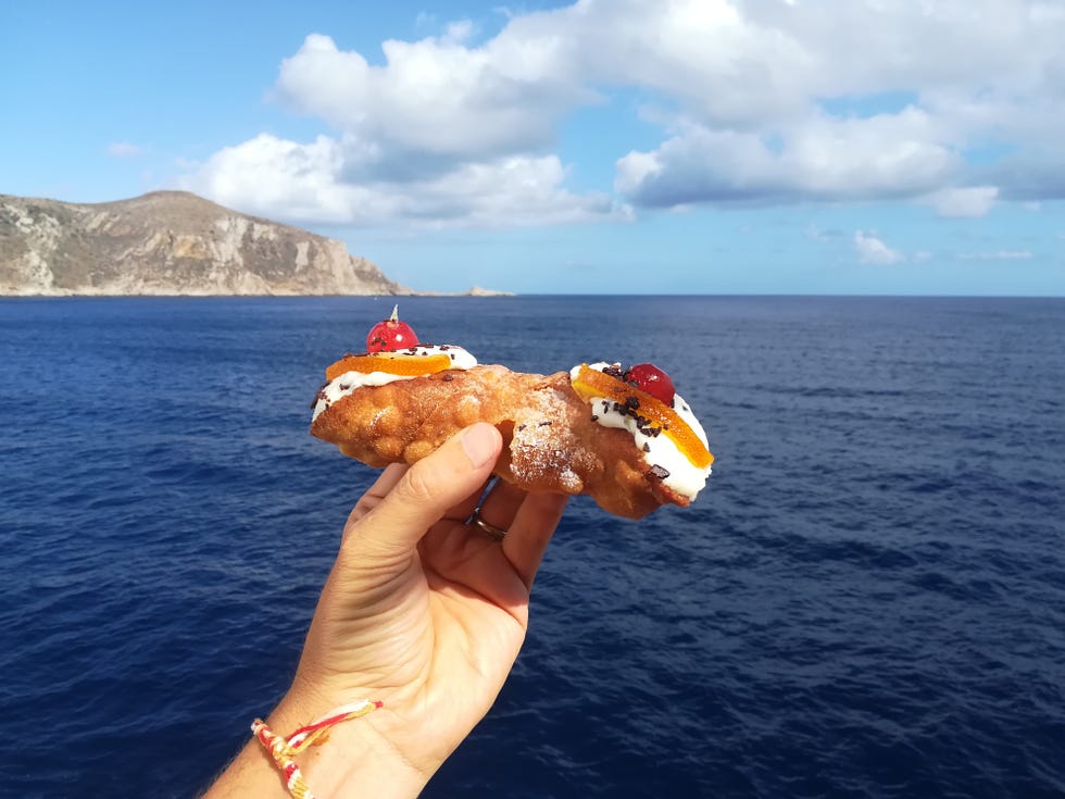 hand with sicilian cannolo with the sea and egadi island in the background