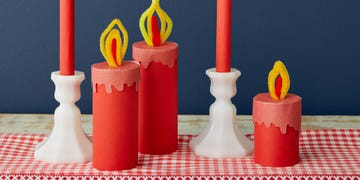 candles made from paper and pipe cleaners on a gingham surface in front of a blue wall