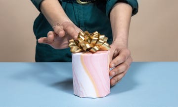 hands adjusting gold bow on gift wrapped candle