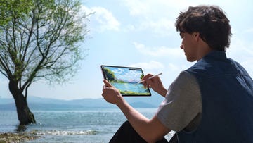 a man sitting down in front of a river drawing using a huawei tablet