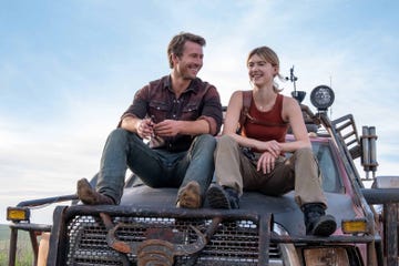 two individuals resting on the hood of a rugged vehicle in an outdoor environment