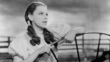 judy garland in a scene from the wizard of oz, she stands in a dress and pigtails and looks to the right