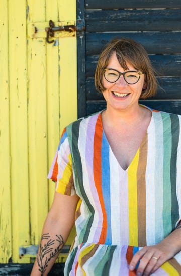 person wearing a multicolored striped dress sitting against a colorful wooden backdrop