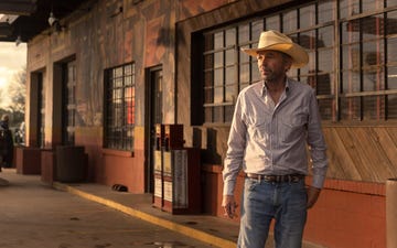 a person wearing a cowboy hat and striped shirt stands near a building with mural artwork