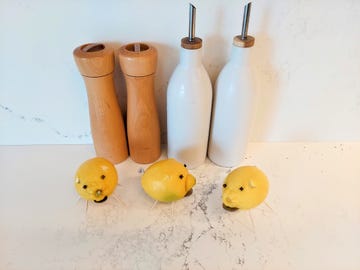 three pigs with lemons for bodies, cloves for eyes, toothpicks for legs, aluminum foil tails and coins in their mouths on a marble counter with kitchen items in the background