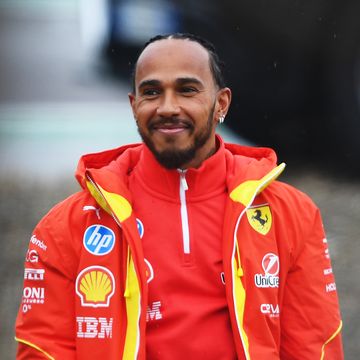 lewis hamilton smiles and looks to the left, he wears a red outfit for his ferrari formula 1 team