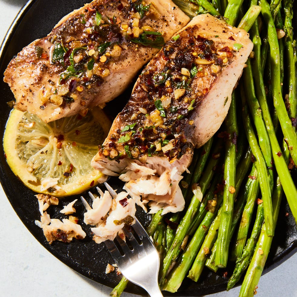 garlicky lemon mahi mahi in a cast iron pan with lemon slices and asparagus