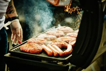 man seasoning burgers and hot dogs on barbecue