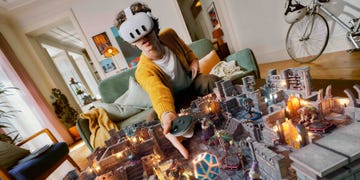 a man playing on the meta quest 3, he wears a white headset and holds a small controller and in front of him is a superimposed virtual castle