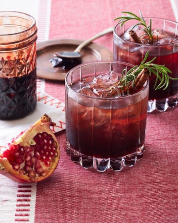 two drinks garnished with herbs and spices alongside pomegranate