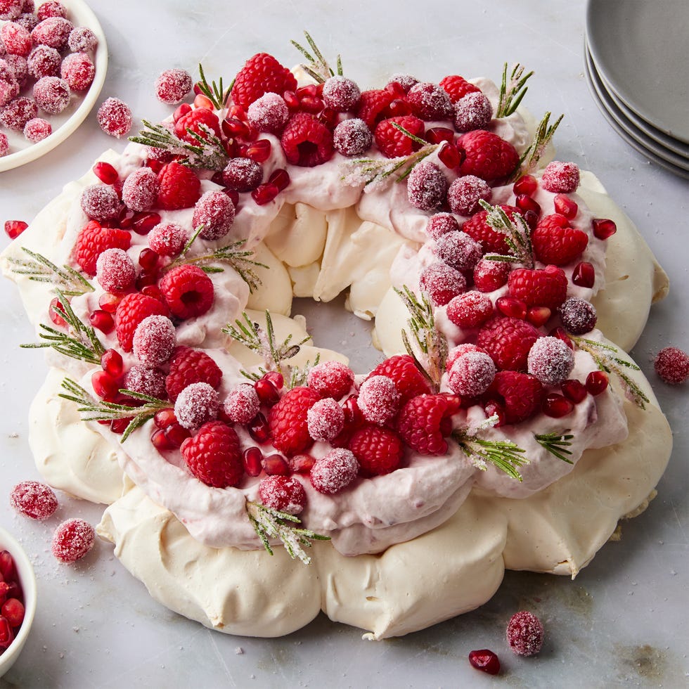 pavlova in a circle topped with sugared cranberries, rosemary, and raspberries