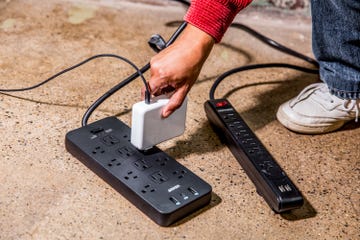 a hand connecting a charging device to a power strip on the ground