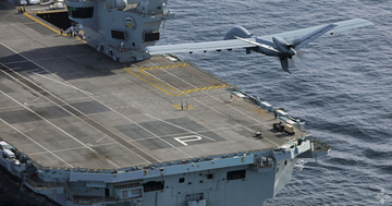 military drone flying above an aircraft carrier at sea