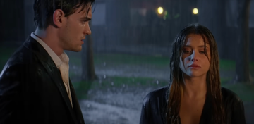 two individuals standing under rain engaged in conversation