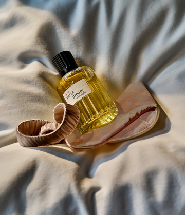 a bottle of perfume and a hair tie arranged on a lightcolored fabric surface