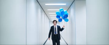 a man in a suit holding blue balloons in a corridor