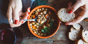 woman eating hearty soup in orange bowl with bread