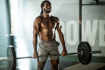 sweaty african american athletic man exercising with barbell in a gym