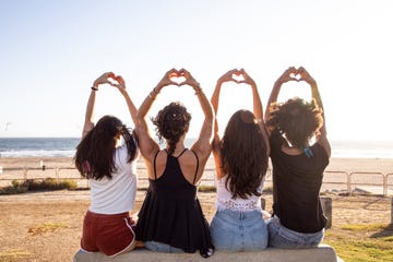 four girls sitting and holding up hands into hearts while looking out on the beach