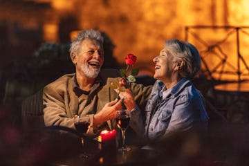 lovely old lady admiring the red flower that her husband gave her while the two have glasses of red wine at a restaurant at night