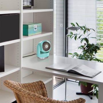 small desk fan on a white shelf next to a plant and an open book