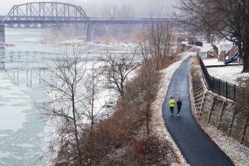 two individuals jogging along a snowcovered path beside a river with a bridge in the background