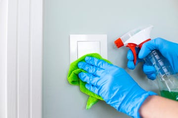 woman cleaning a light switch with a disinfecting spray