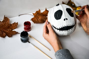 woman paints face on orange pumpkin for halloween autumn leaves diy children craft do it yourself