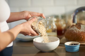 woman pouring oats into bowl in kitchen, close up