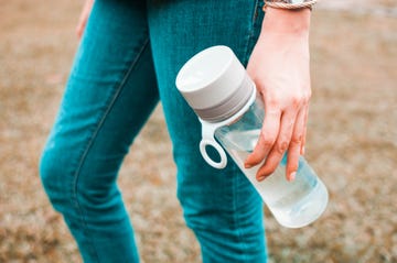 a young woman is holding a reusable water bottle container outdoors