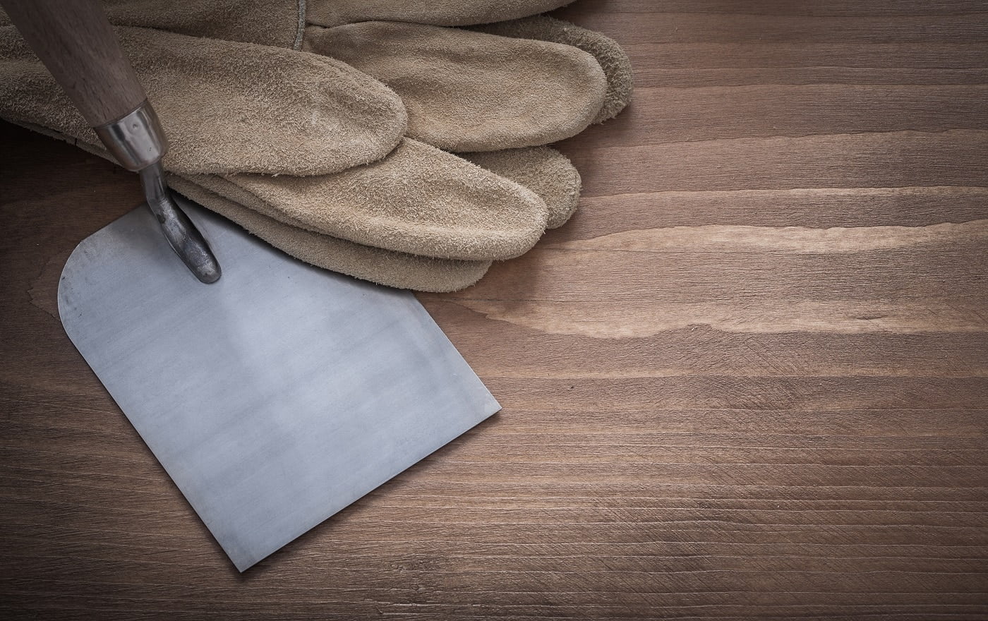 Construction safety gloves and bricklaying trowel on wooden background.